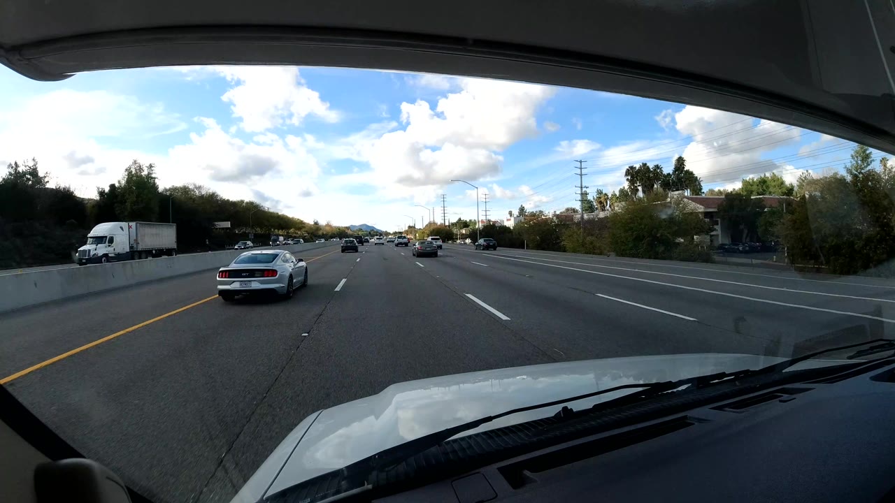 Freeway lanes with cars ahead, trees on the roadside, and a white box truck at left.