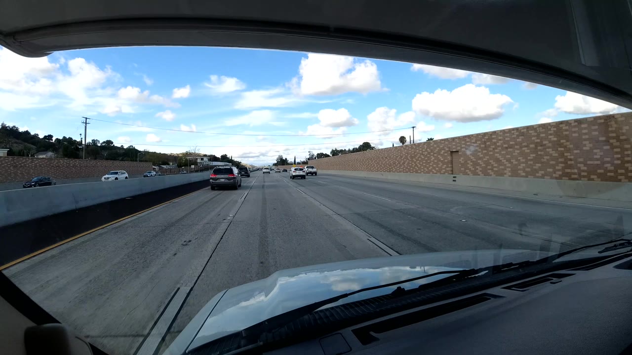 Cars travel on a multilane freeway beside a tan wall.