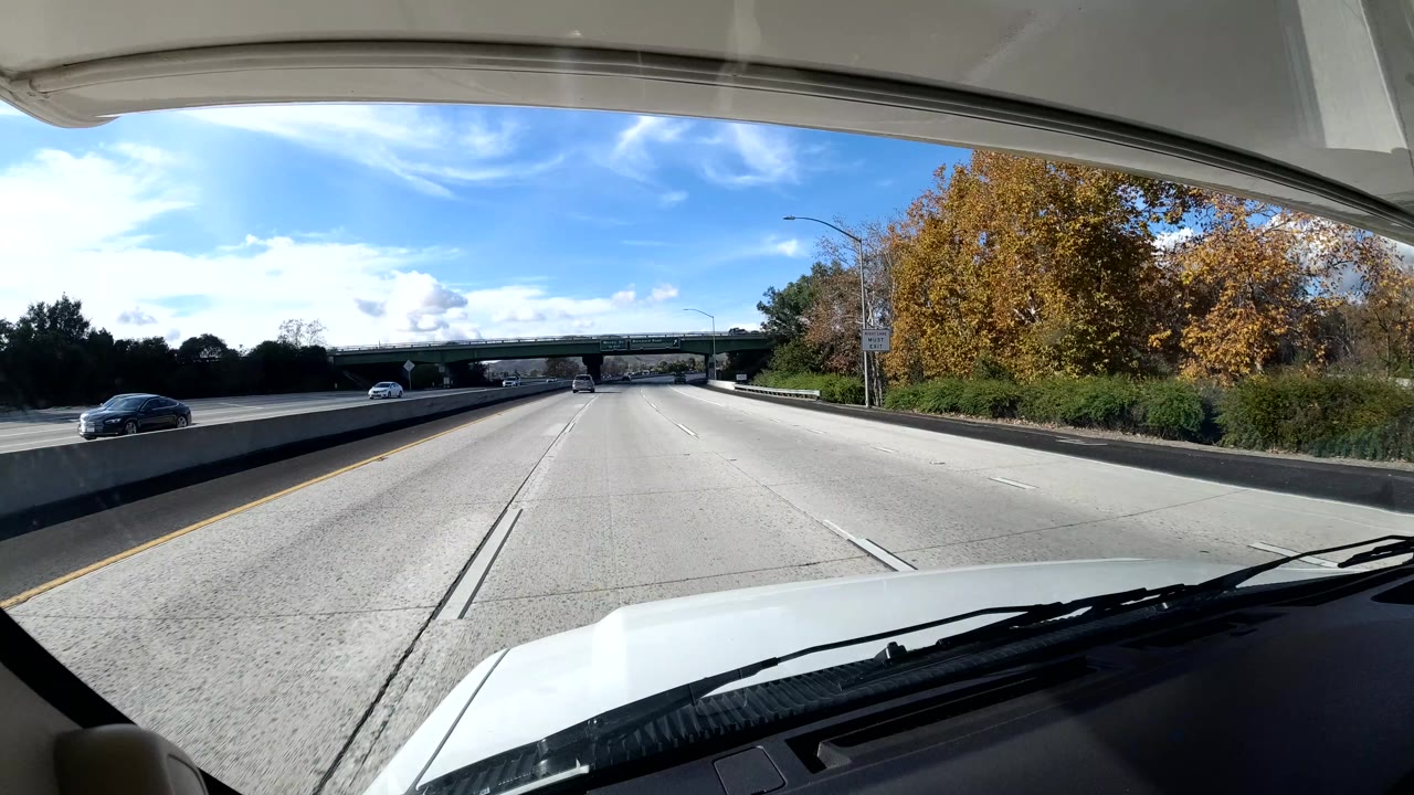 Open freeway lane with an overpass ahead and autumn-colored trees at right.