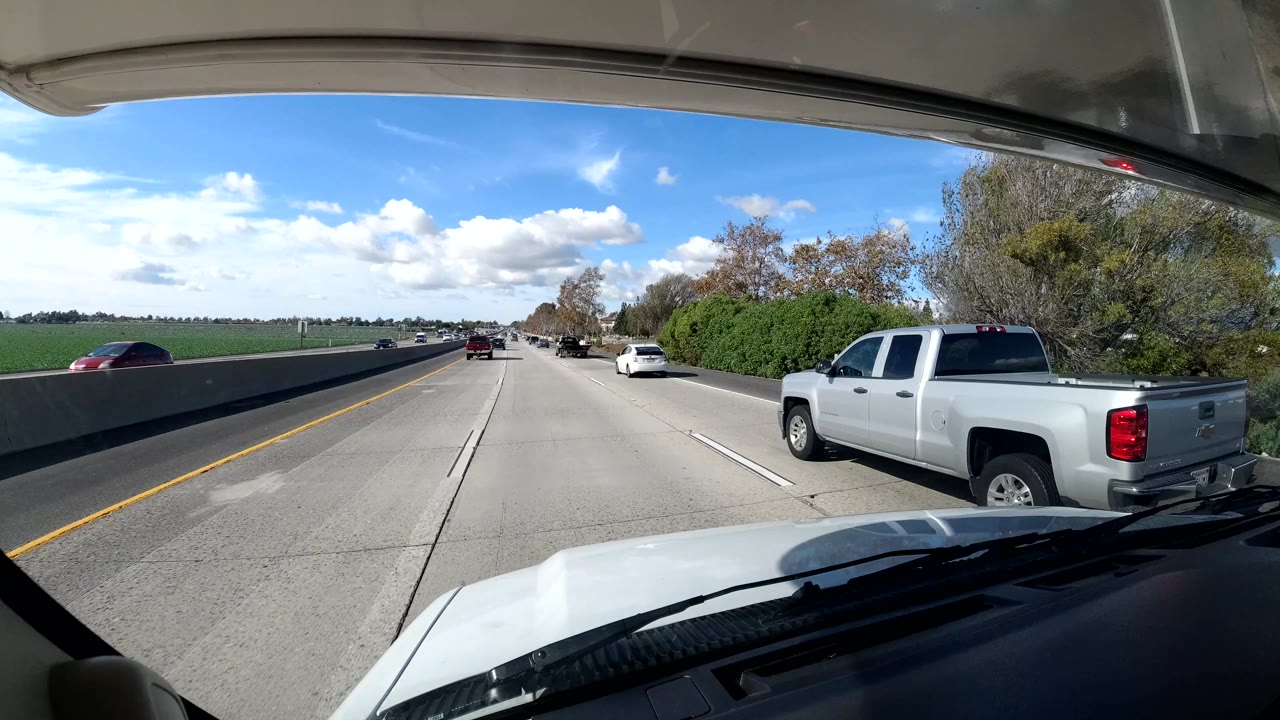 Highway view with a white pickup in the adjacent lane and flat land beyond the barrier.