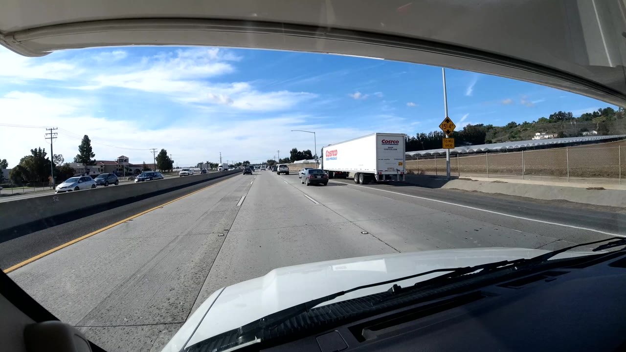 Forward-facing vehicle view on a Central Coast California freeway with a Costco truck ahead to the right, roadside retaining wall, blue sky, and no visible people.