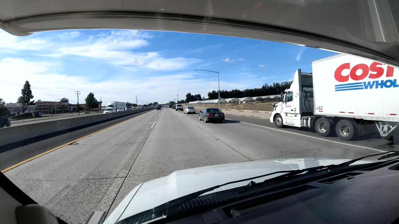Large Costco truck passing beside freeway traffic from a windshield view.
