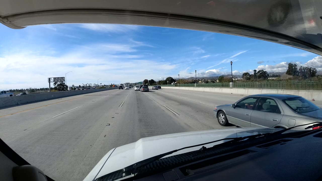 Freeway view with a gray sedan passing near the vehicle and mountains beyond the lanes.