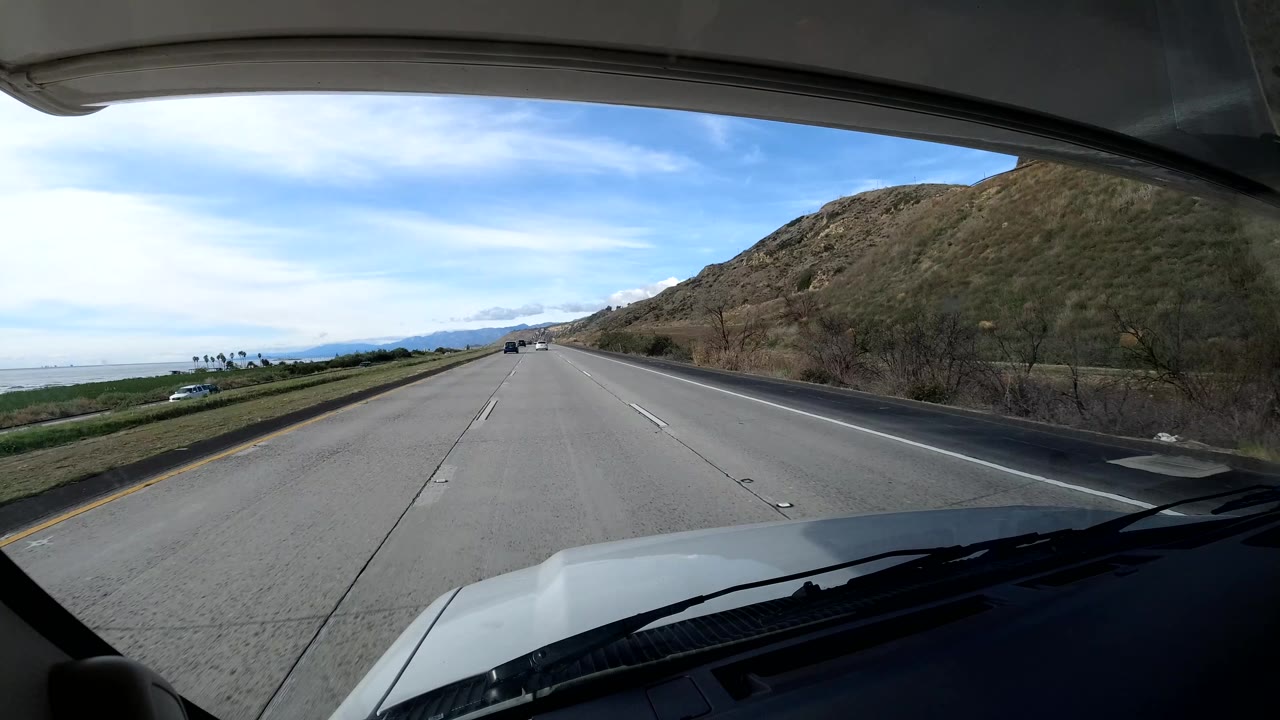 Wide highway lanes with ocean on the left and dry hill on the right.