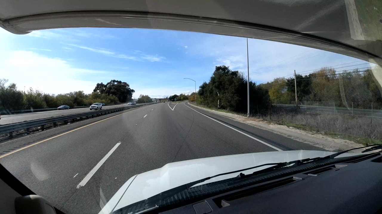 Highway view through a windshield with a car on the opposite side and trees along the shoulder.