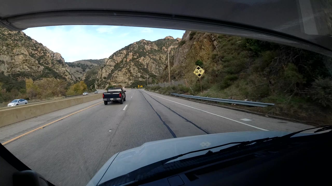 Highway lane through a rocky canyon area with a pickup truck ahead.