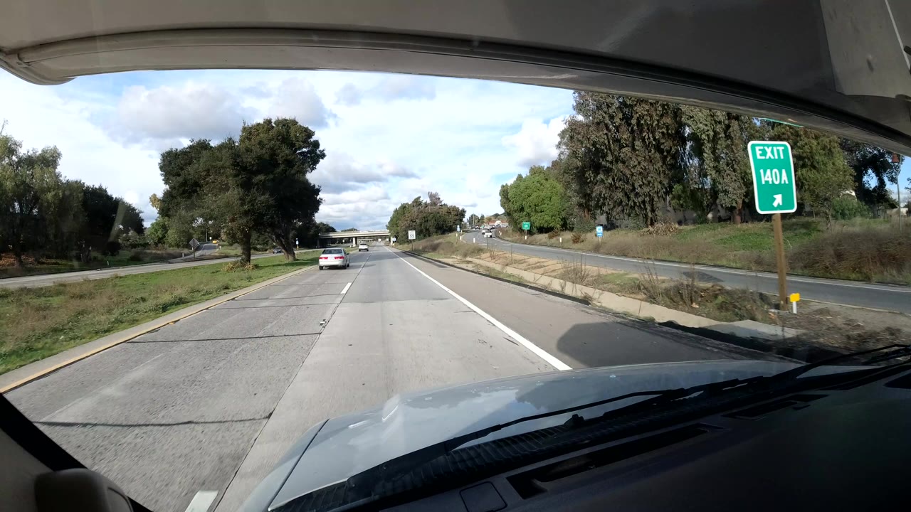 Highway exit sign beside lanes with trees and a car ahead.
