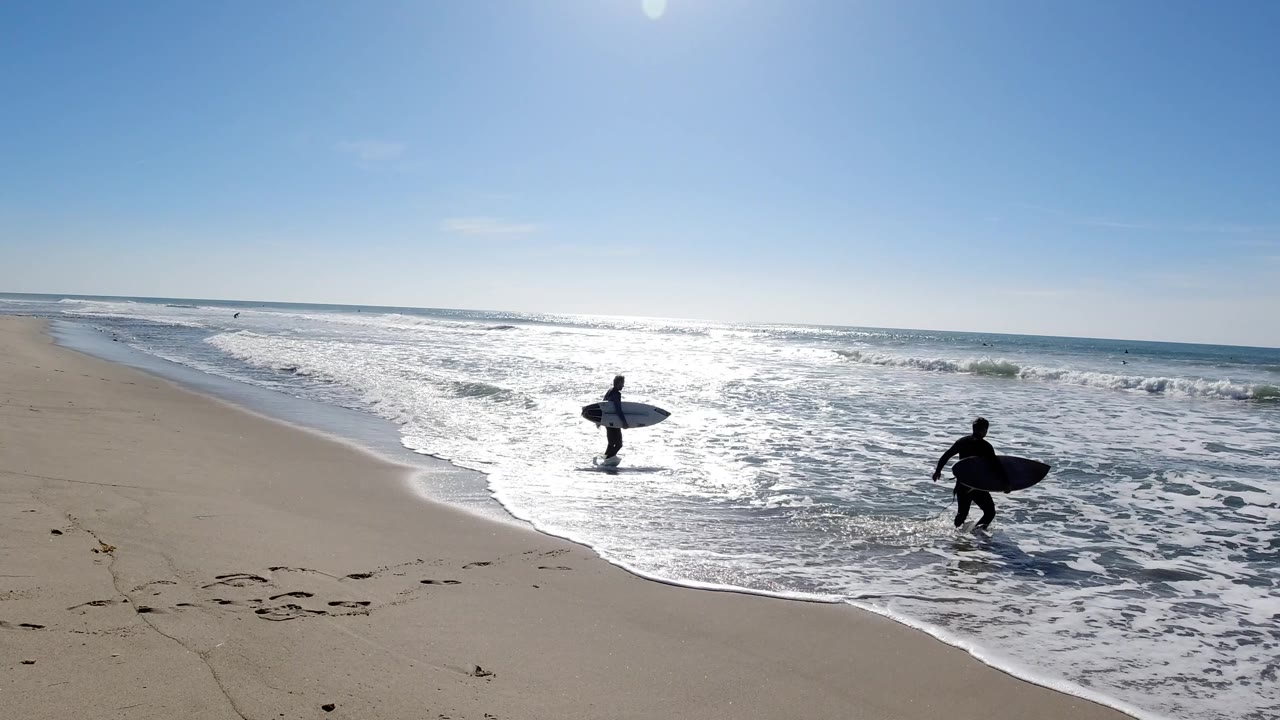 Surfers at the waterline with sun glare across the ocean
