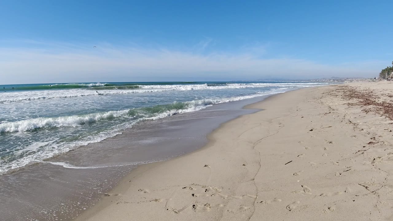 Trestles Beach shoreline with a low band of foamy surf advancing toward wet sand, open beach stretching right, and no visible people in this frame.