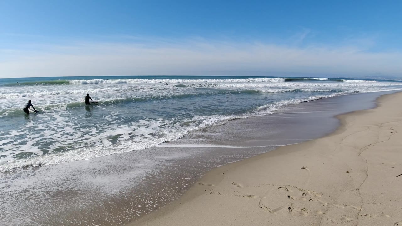 Two people wading in shallow surf along a sandy beach.