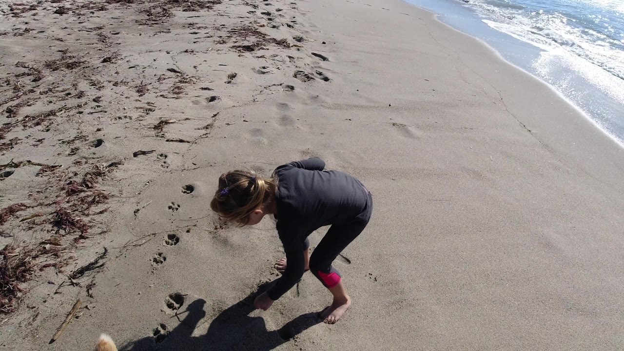 Young girl crouched on sand beside beach footprints.