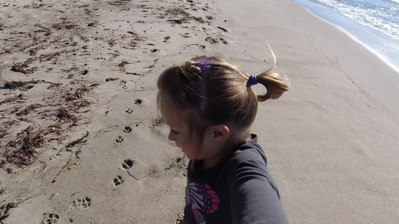 Young girl in profile on sand beside the ocean.