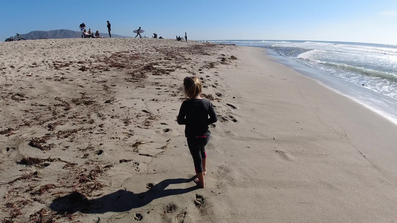 At Trestles Beach, California, the child walks closer to the right side of frame while a long shadow stretches across the sand toward the ocean.