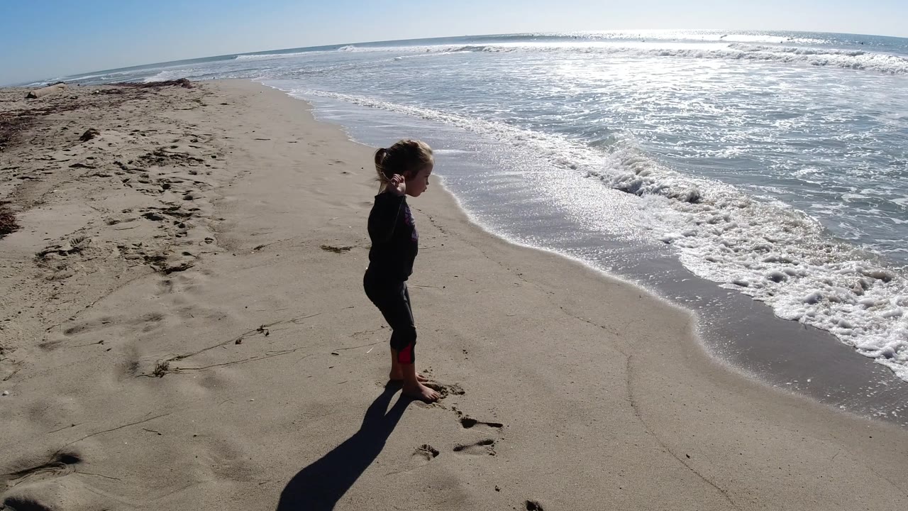 The child remains in profile on the Trestles Beach shoreline as a curved band of white foam reaches the wet sand.