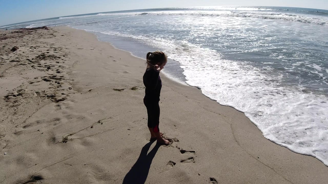 At Trestles Beach, California, the child stands near the lower left while a larger sheet of foamy water spreads across the shoreline.