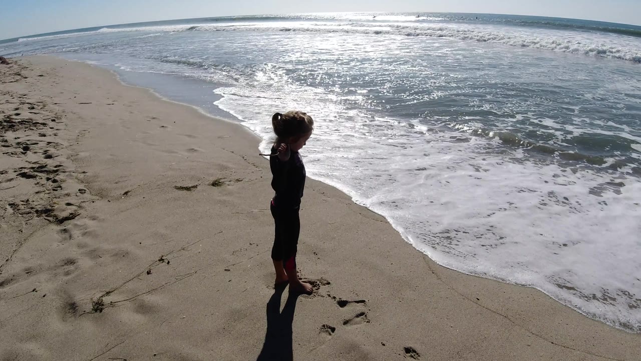 Child near foamy surf with footprints in the sand.