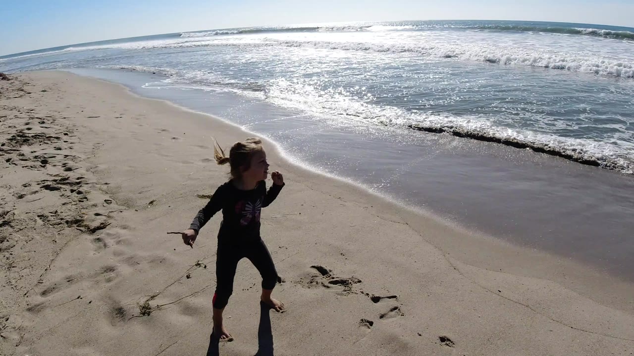 Girl holding a stick on sand beside the surf line.