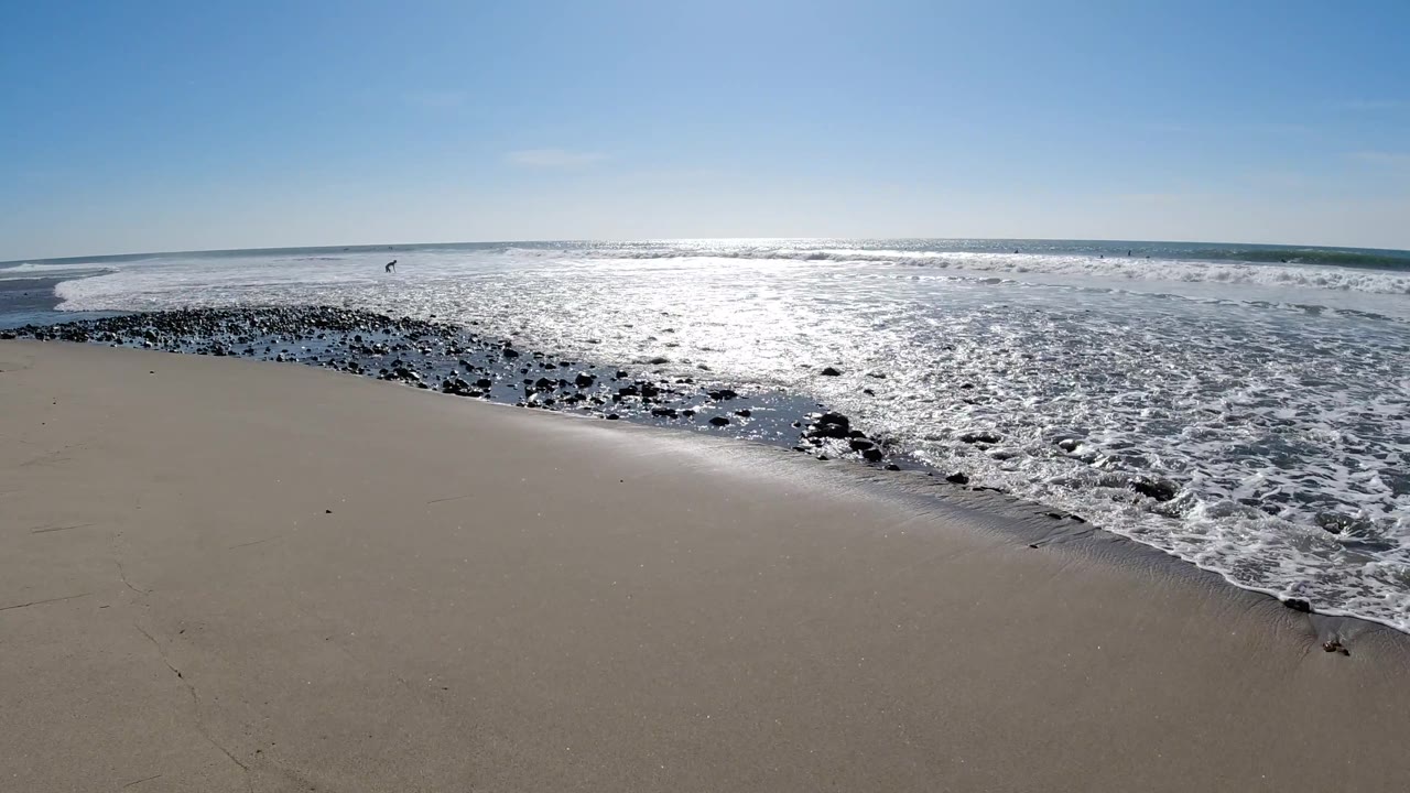 Wide pale sand beach at Trestles Beach, California, with white wave foam curving across the midground, glinting sun-lit water, and no visible people