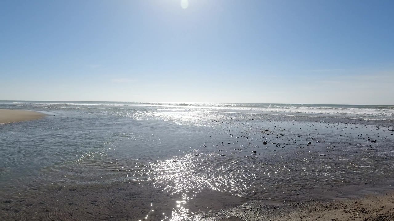 Sunlit tidal flat wide angle at Trestles Beach, California, with strong specular glare on shallow water, ocean in background, and clear blue sky; no visible people