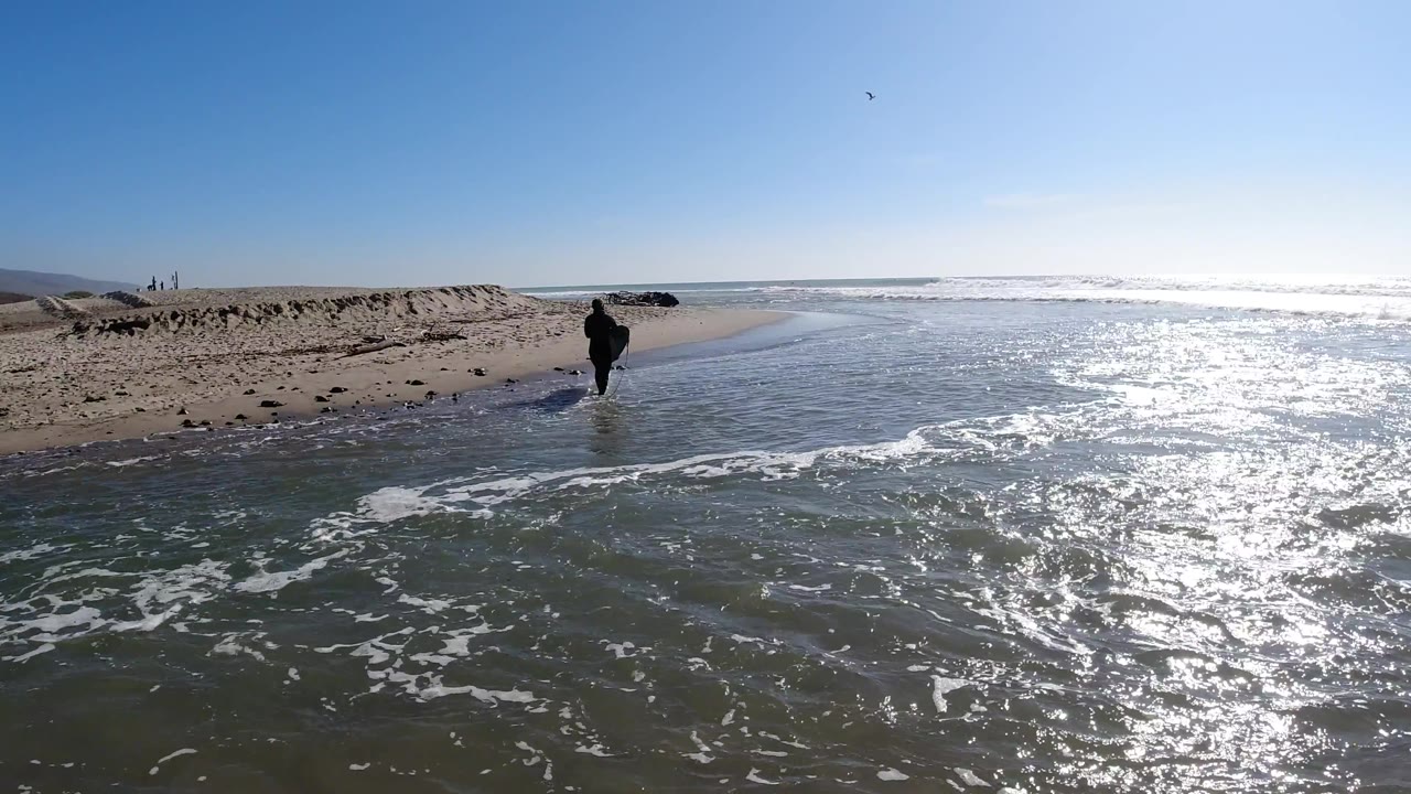 At Trestles Beach, California, the man appears slightly farther from the camera as rippled shallow water and bands of white foam fill the foreground.