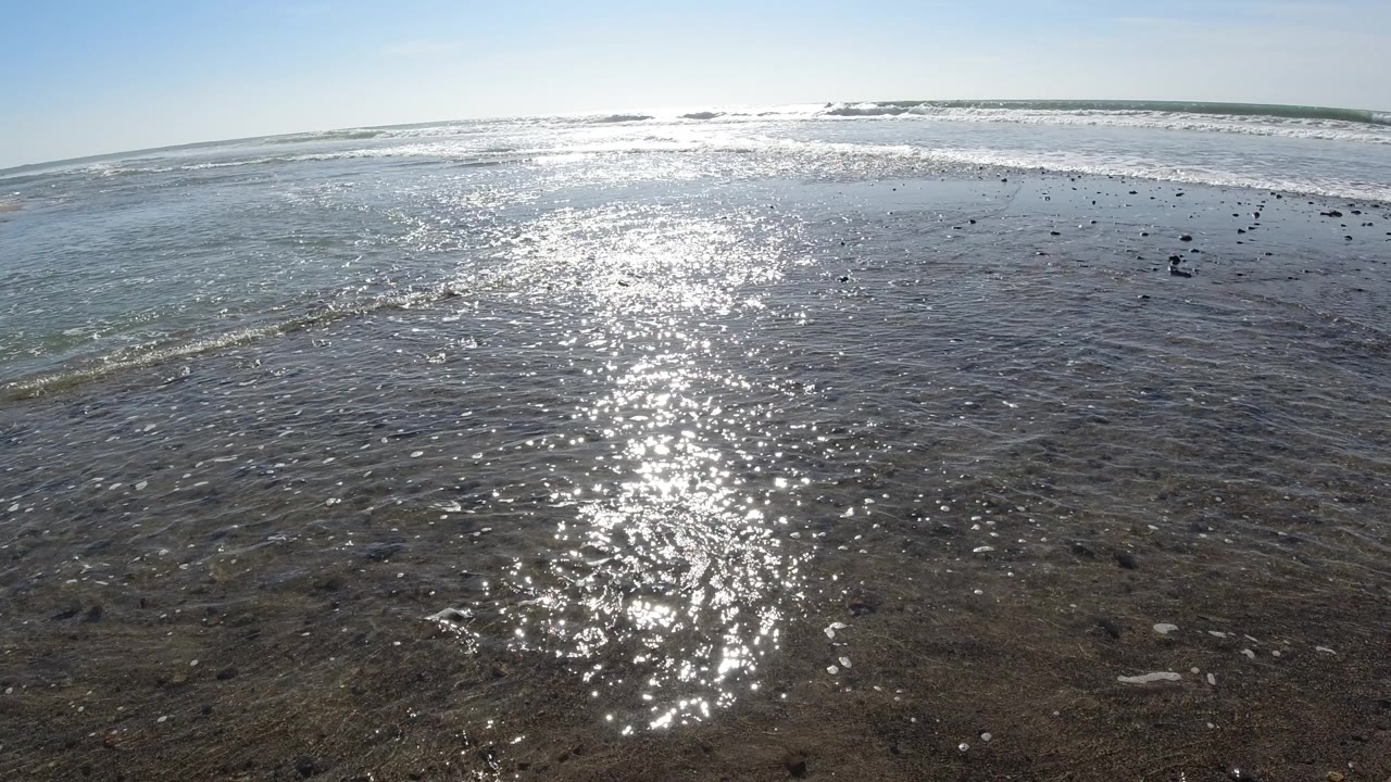 At Trestles Beach, California, bright sun reflection runs down shallow rippled ocean water toward distant breaking waves, with no visible people.
