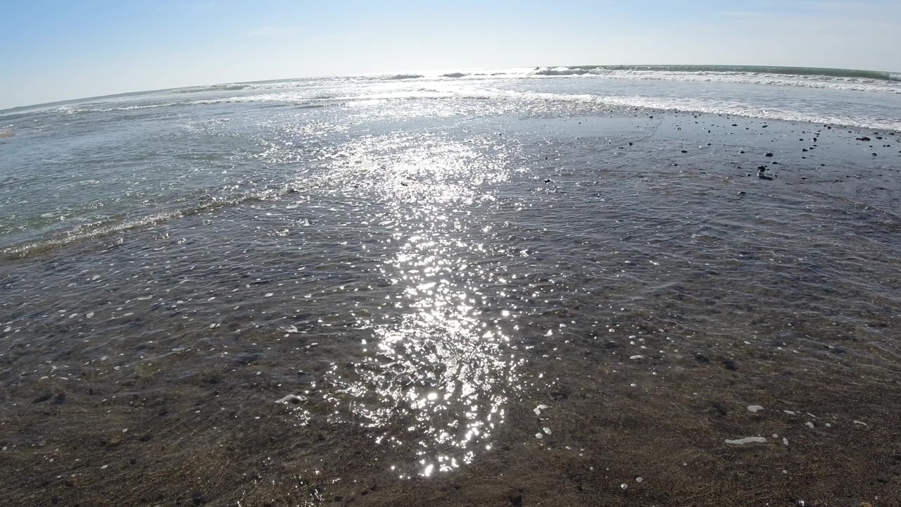 Bright reflected sunlight across rippled ocean water and low surf.