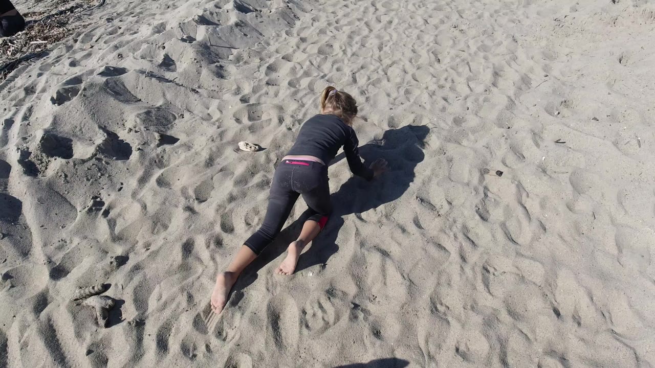 Child low to the sand with footprints and ridged sand nearby.