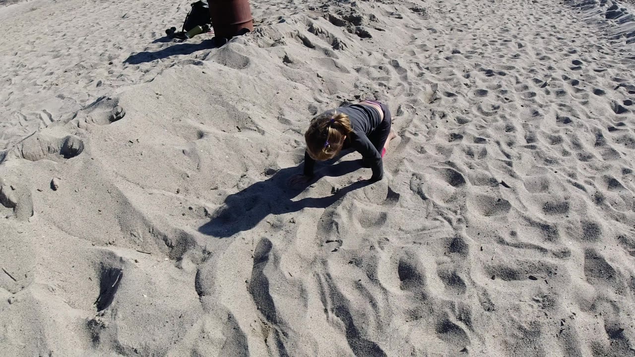 At Trestles Beach, California, the child has shifted slightly right in the overhead view, with a dark body shadow stretching across the open sand.