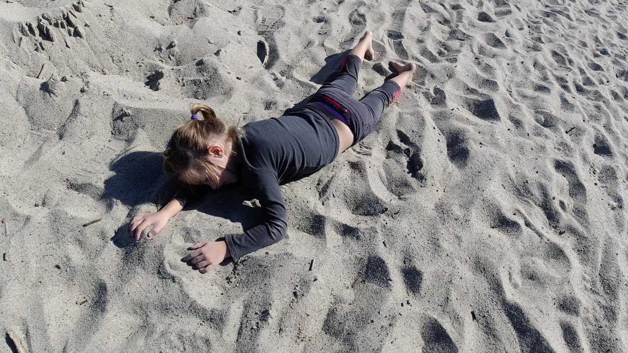 Child stretched out on sand with one hand near a small mound.