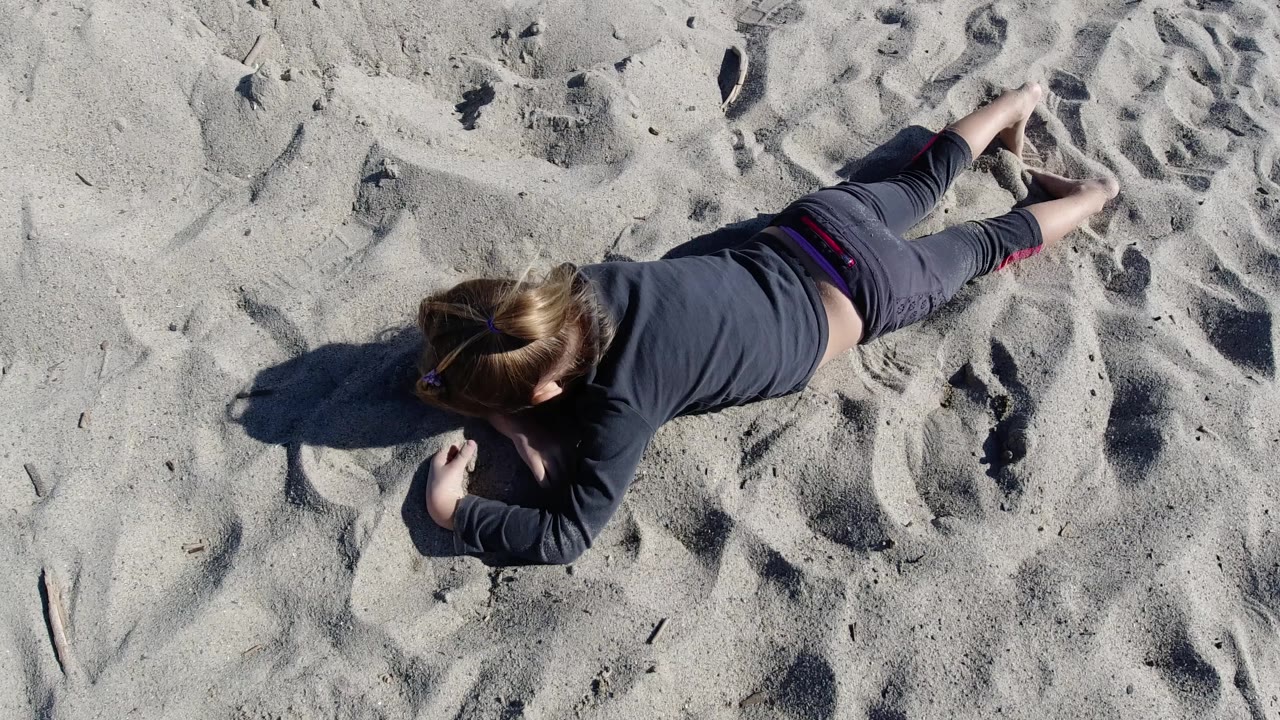 Child resting on sand with arms folded near her head.