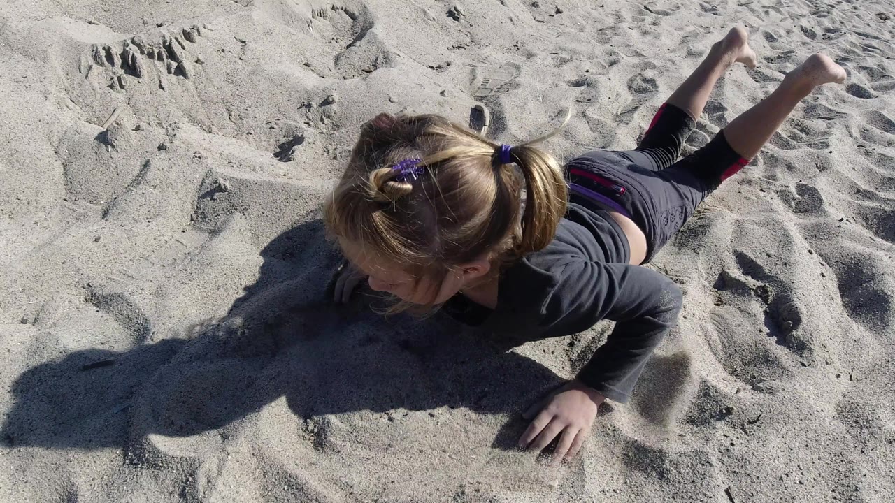 At Trestles Beach, California, the girl pushes up on her hands with her head turned down toward the sand and her legs extended behind her.