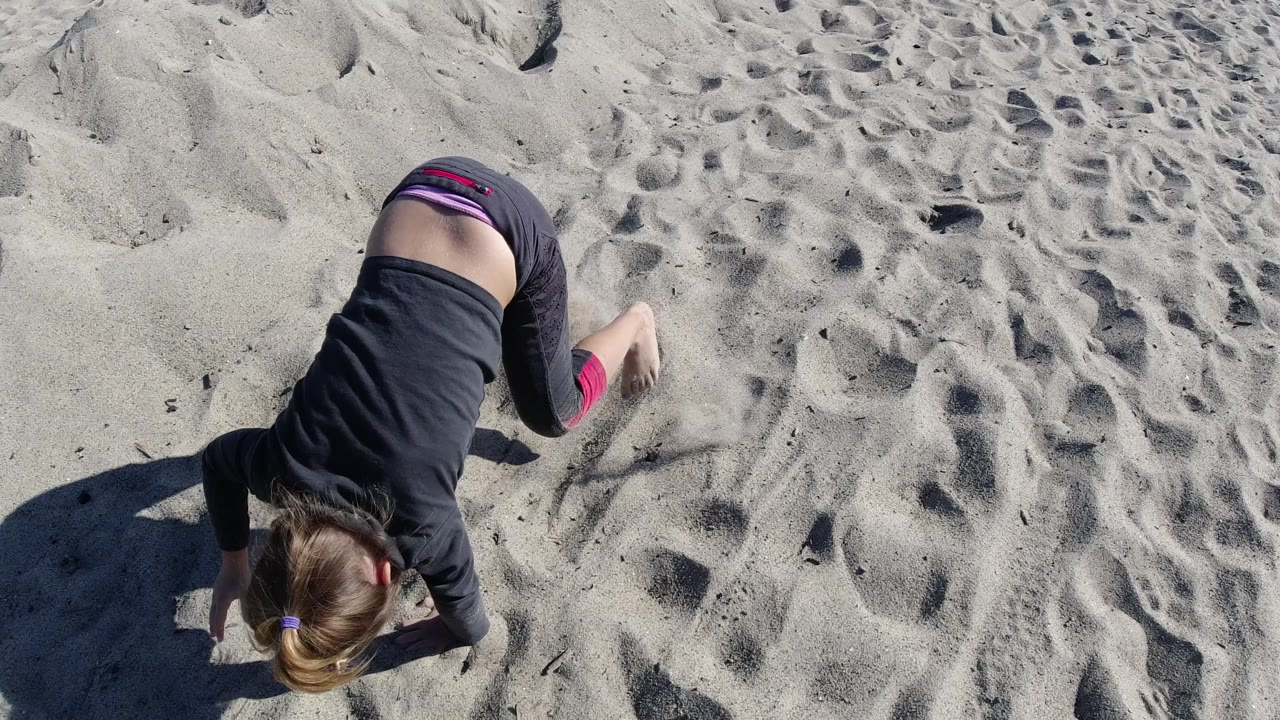 At Trestles Beach, California, the child shifts forward on her hands with footprints and small sand ridges filling the frame.