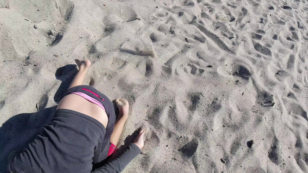 Girl partly cropped while lying on sandy beach ground.