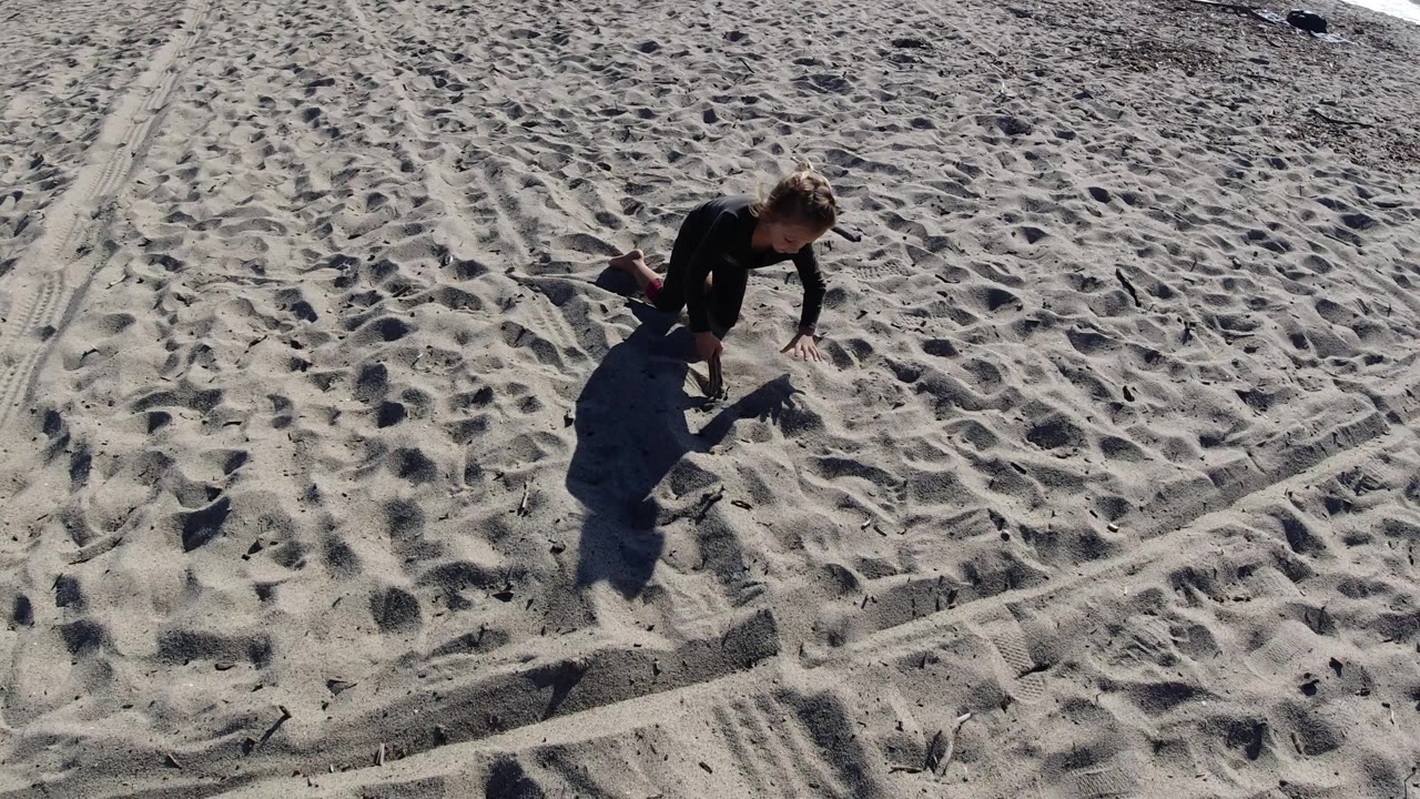 At Trestles Beach, California, the young girl appears farther to the upper right of the sandy frame, with her dark clothing and shadow standing out against footprints and diagonal track marks.