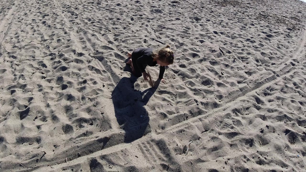 Young girl crouched on beach sand with footprints and shadows.
