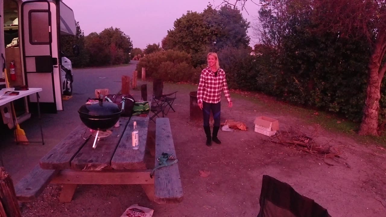 Woman faces the camera near a picnic table and grill.