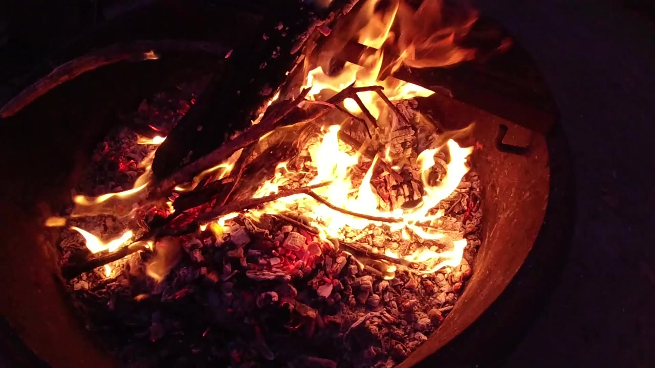 Tall orange flames curl around blackened wood above glowing coals.