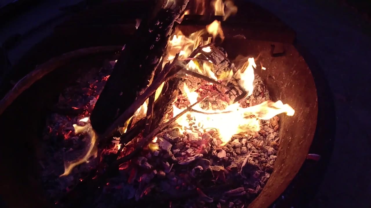 Round metal fire barrel viewed from above with active flames and sticks burning inside, dark night setting