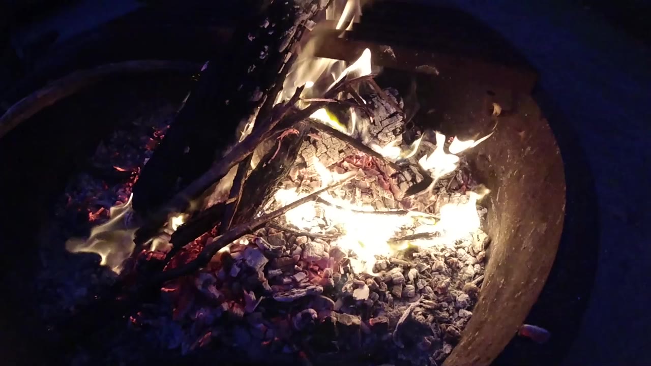 Overhead view of a round metal fire pit burning at night with bright flames and red-orange embers