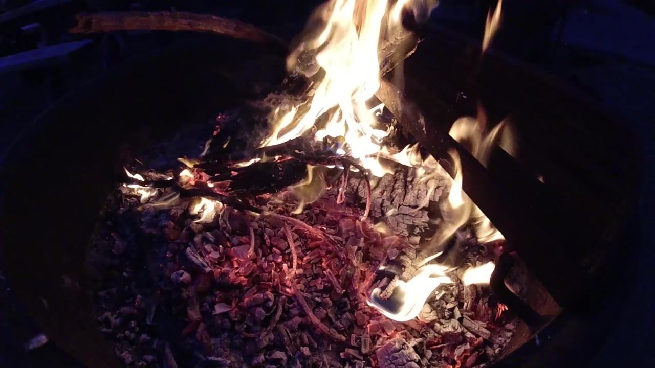 Flames flare above charred wood and glowing coals.