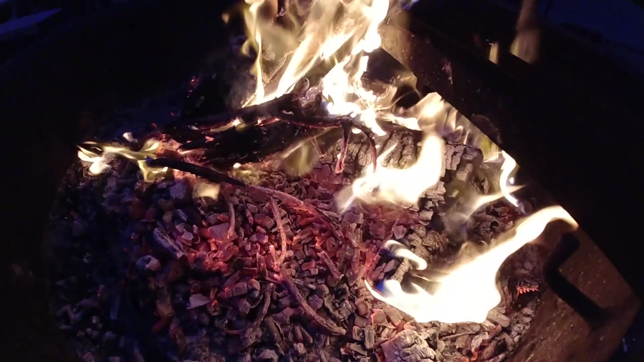 At three seconds, a large flame rises prominently on the left side of the frame with intense ember activity spread across the burning pile and completely dark surroundings; no people visible.