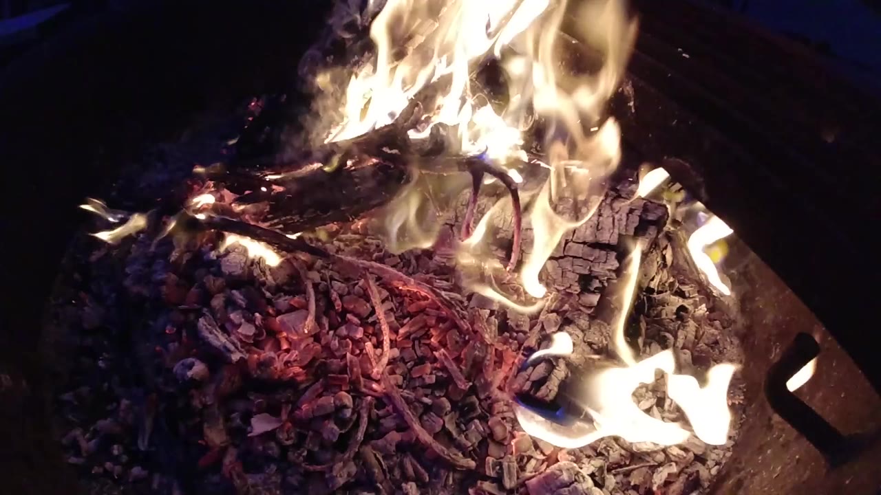 Overhead campfire with orange flames rising upper-left and a bed of red and purple glowing embers