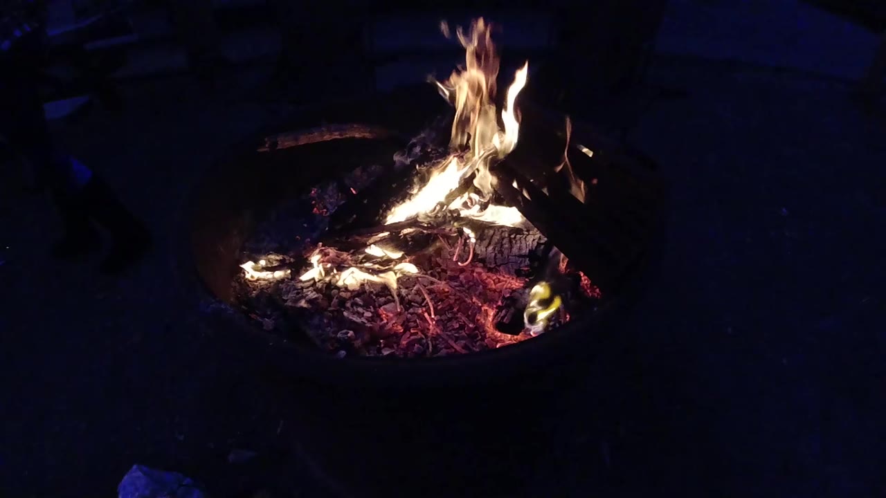 Campfire in a metal fire ring with flames spreading wider, glowing embers below