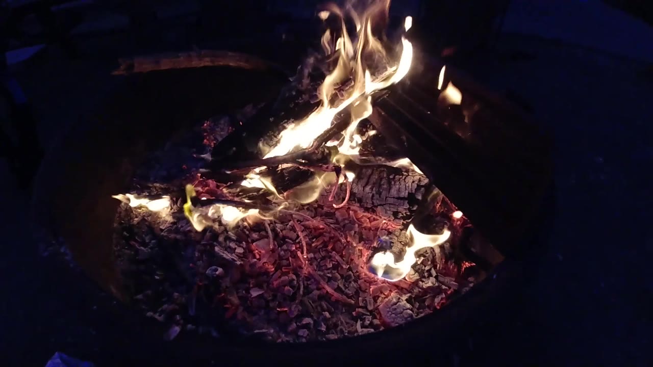 Close-up of burning debris and flames inside a dark metal fire container