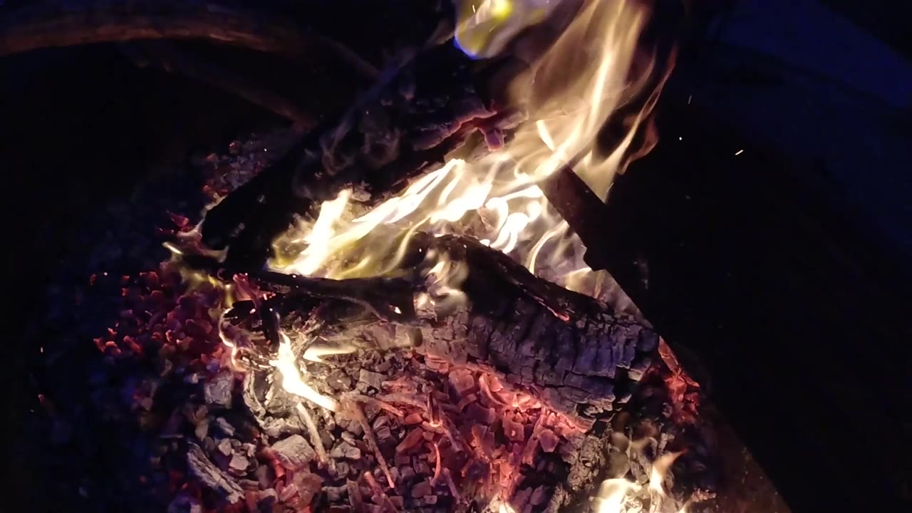 One second into the clip at Trestles Beach, California, the campfire holds its height but the flame has shifted in shape, leaning slightly and showing more of the glowing ember bed below; no people are visible