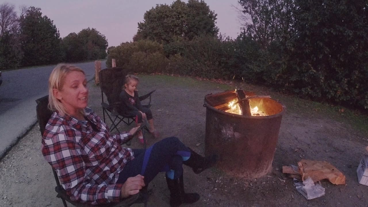 The woman turns her face toward the child while the fire ring burns on the right and dark trees fill the background at Trestles Beach, California.