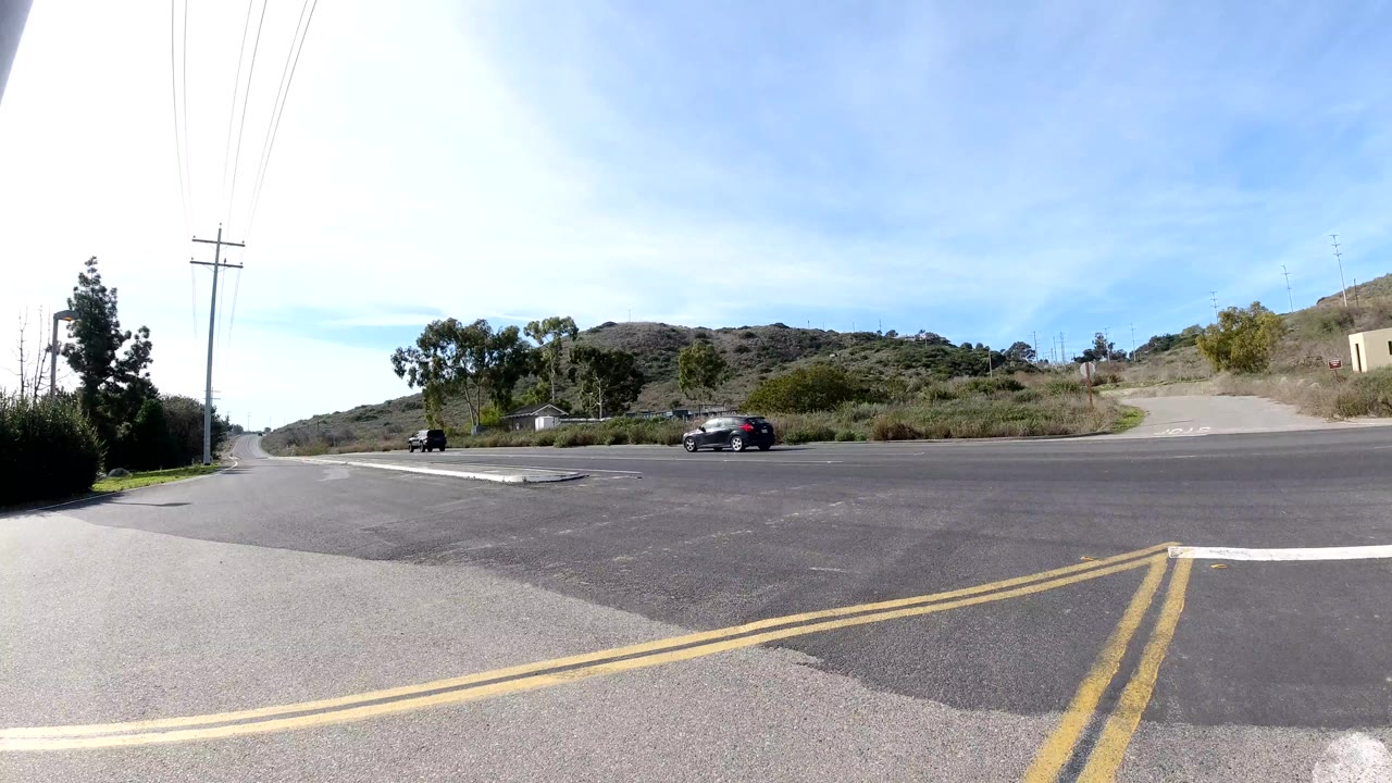 Intersection with double yellow lines, utility poles, hills, and a passing car.