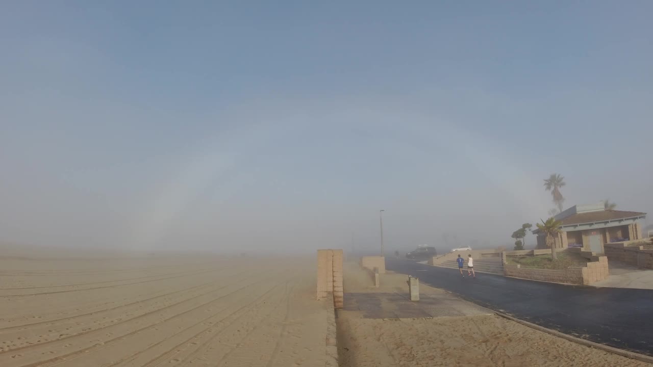 Beach path and low wall with two people receding into windblown sand.