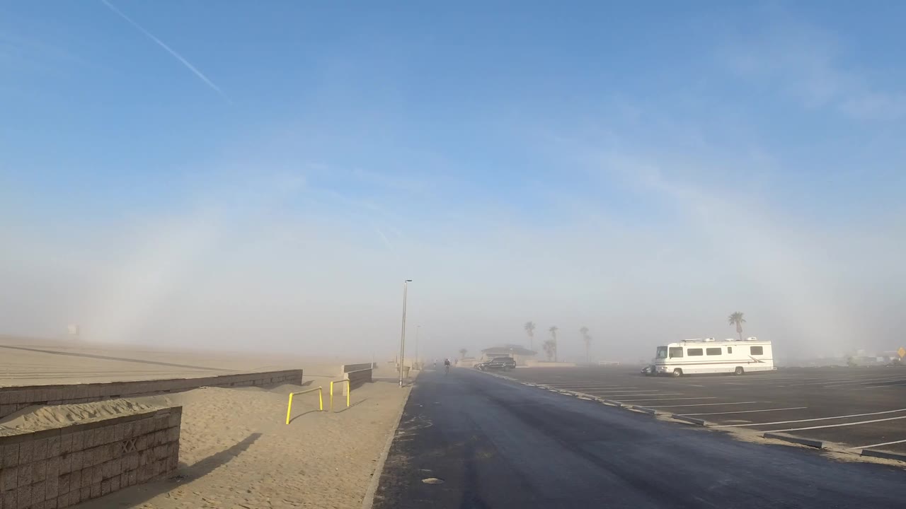 Roadside landscape with low wall, yellow bollards, haze, blue sky, and white van.