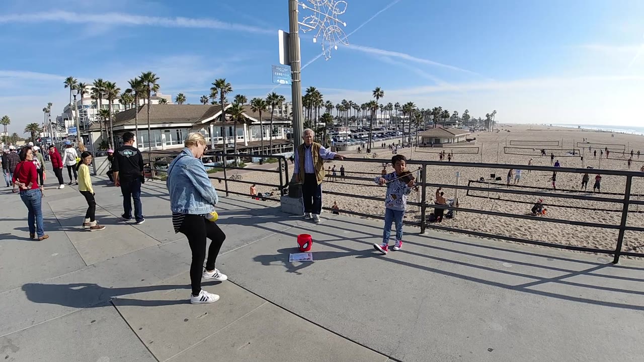 Promenade onlookers face a young boy performing near the beach railing.